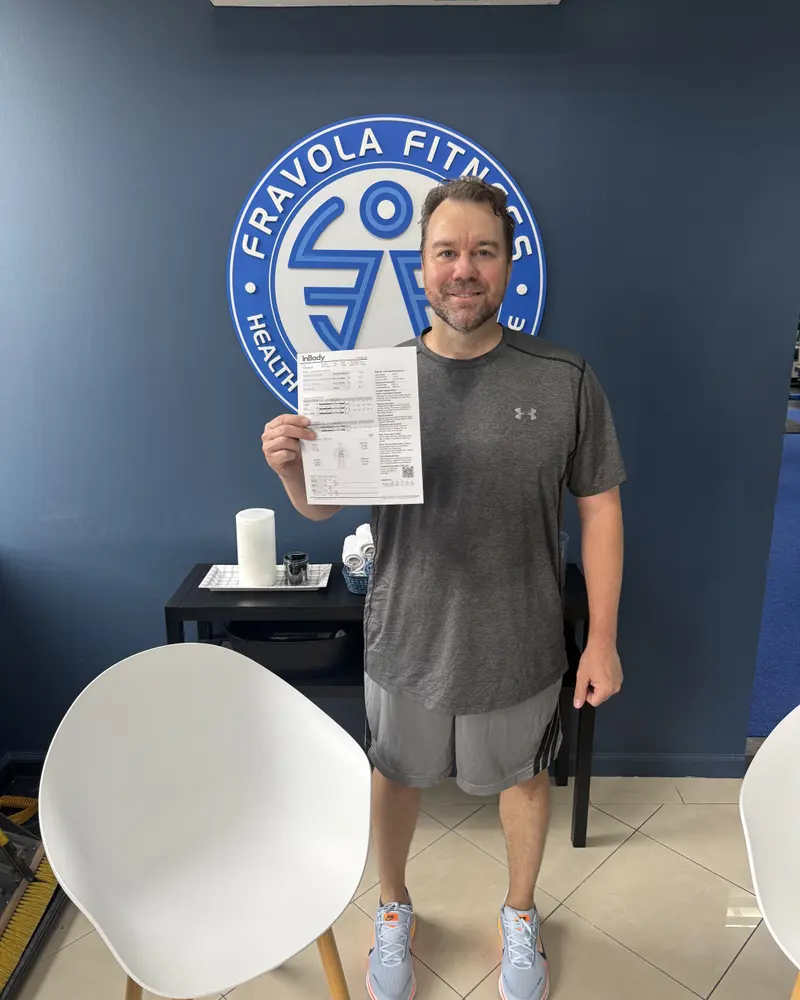 A member with their results in front of the Fravola Fitness logo wall